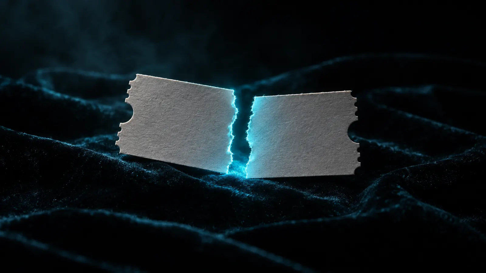 A blank paper ticket torn in half on dark velvet, cyan light glowing along the torn edge.